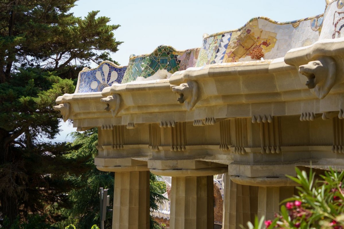 A stone viaduct of leaning mosaic columns winding through Park Guell