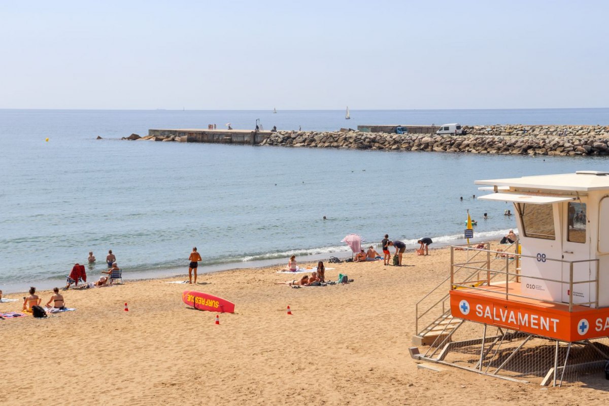 Sunbathers on a Barcelona beach beside a lifeguard tower under a blue sky
