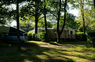 A wooden mobile home and a campervan on a shaded pitch at a campsite in France