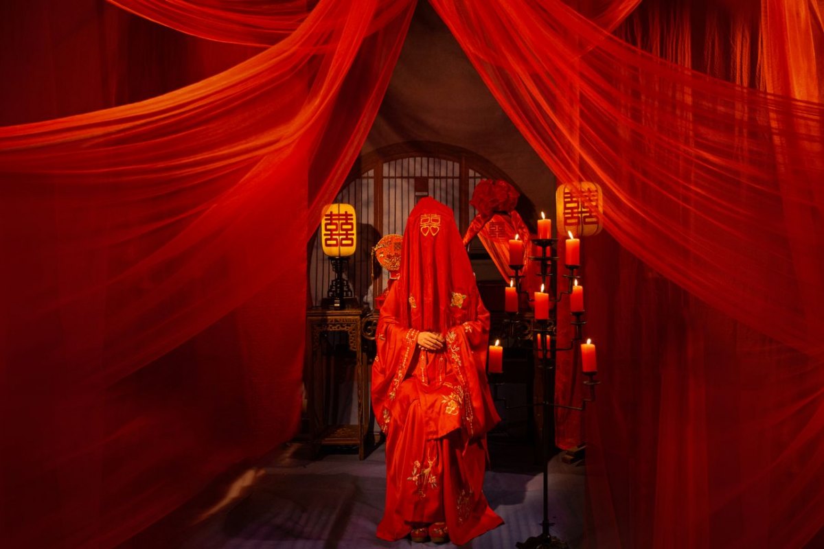 A bride in red beneath Double Happiness symbols at a traditional Chinese wedding