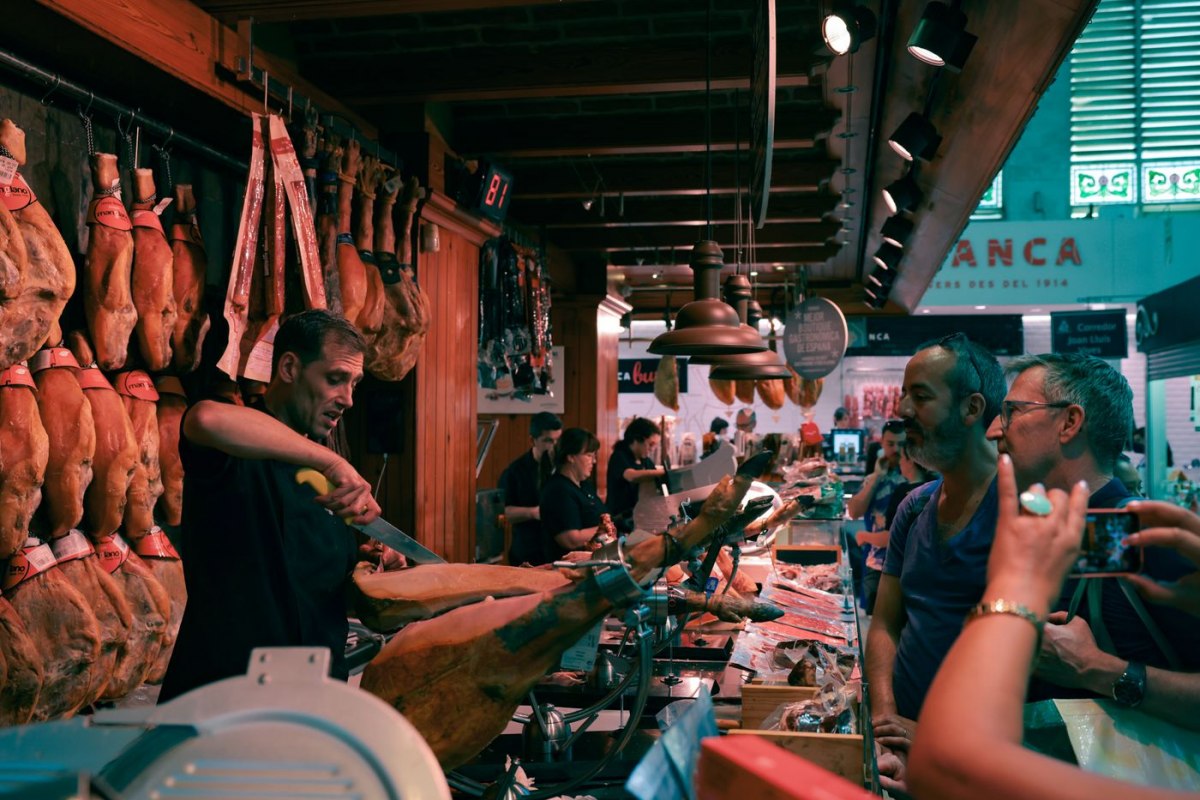 A vendor hand-slicing cured Spanish jamon at a Barcelona market counter