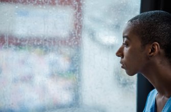 A woman sitting by a rain-streaked window looking away, feeling homesick