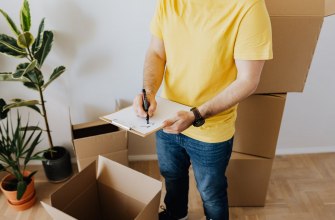 Person ticking off a checklist on a clipboard beside packed moving boxes