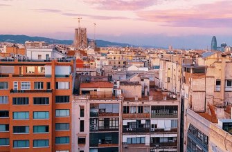 A rooftop terrace looking over Barcelona residential blocks toward the Sagrada Familia at sunset